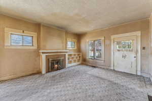Unfurnished living room featuring carpet flooring, a textured ceiling, and a glass covered fireplace
