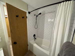 Full bathroom featuring a textured wall, tile patterned flooring, and shower / tub combo