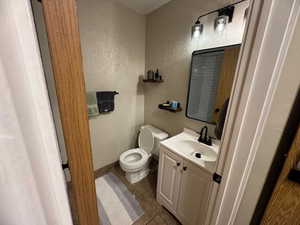 Half bath featuring tile patterned floors, baseboards, vanity, toilet, and a textured wall
