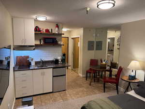 Kitchen with under cabinet range hood, white cabinetry, refrigerator, and tasteful backsplash