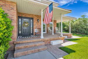 Property entrance with covered porch, brick siding, and a lawn