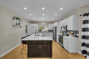 Kitchen featuring white cabinetry, appliances with stainless steel finishes, a sink, and a kitchen bar