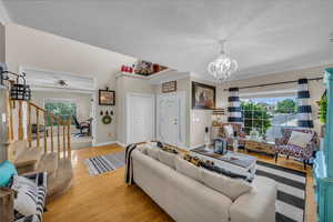 Living room with a textured ceiling, crown molding, a notable chandelier, light wood-style floors, and stairs