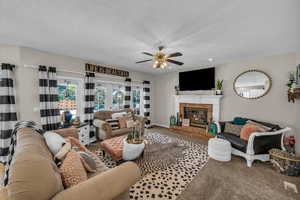 Carpeted living room with baseboards, ceiling fan, a brick fireplace, and a textured ceiling