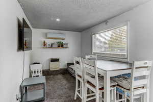 Dining area with heating unit, a wall unit AC, carpet, and a textured ceiling