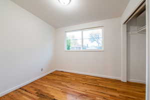 Unfurnished bedroom featuring vaulted ceiling, baseboards, a closet, and light wood-style flooring