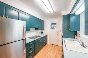 Kitchen with black electric stovetop, a sink, light countertops, freestanding refrigerator, and decorative backsplash