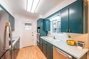 Kitchen featuring a sink, light countertops, stainless steel appliances, light wood-type flooring, and ornamental molding