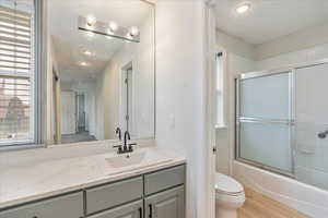 Bathroom featuring vanity, wood finished floors, toilet, recessed lighting, and combined bath / shower with glass door