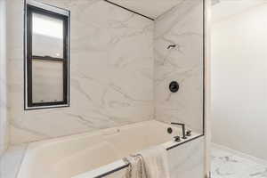Bathroom featuring baseboards, marble finish floor, and washtub / shower combination