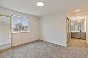 Unfurnished bedroom with light colored carpet, a sink, baseboards, and ensuite bathroom