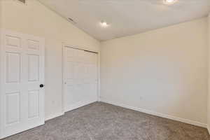 Unfurnished bedroom featuring visible vents, a closet, baseboards, carpet, and vaulted ceiling