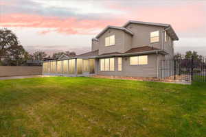 Back of property with a sunroom, a lawn, and fence