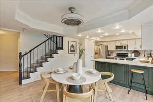 Dining room featuring ornamental molding, a raised ceiling, light wood finished floors, and stairs