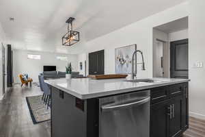 Kitchen with stainless steel dishwasher, dark wood-style flooring, an island with sink, light countertops, and a sink