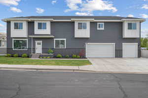 View of front facade with board and batten siding, an attached garage, driveway, and a front lawn