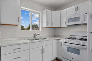 Kitchen with a sink, light countertops, white cabinets, and white appliances