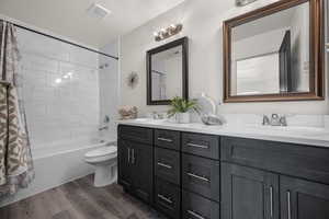 Full bathroom featuring double vanity, a sink, shower / tub combo, and wood finished floors
