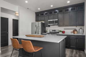Kitchen with a kitchen island with sink, visible vents, light countertops, stainless steel appliances, and dark wood-type flooring