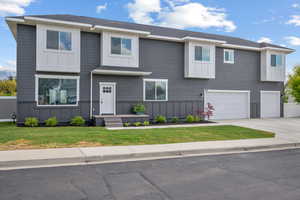 View of front of property with board and batten siding, an attached garage, driveway, and a front lawn