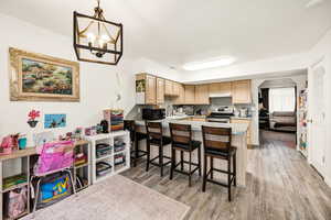 Kitchen featuring a kitchen breakfast bar, stainless steel range with electric cooktop, light brown cabinets, under cabinet range hood, and new laminate tile flooring