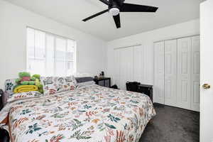 Bedroom with ceiling fan, multiple closets, and dark carpet
