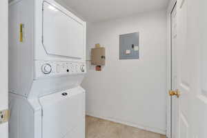 Clothes washing area featuring baseboards, electric panel, stacked washer / dryer, and laundry area