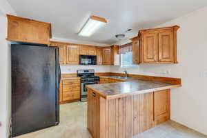 Kitchen featuring brown cabinets, a sink, a peninsula, visible vents, and black appliances