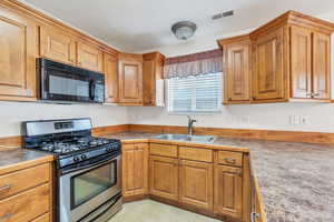 Kitchen with visible vents, brown cabinetry, stainless steel gas stove, black microwave, and a sink
