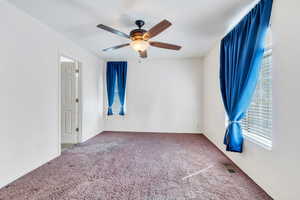 Carpeted empty room featuring ceiling fan, visible vents, and baseboards