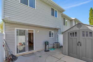 Rear view of property with a storage shed, an outbuilding, cooling unit, fence, and a patio