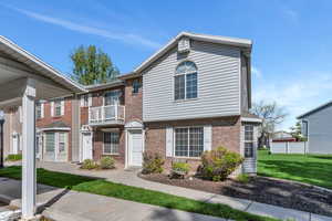 View of property with a balcony, a front yard, and brick siding