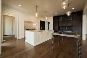 Kitchen featuring light countertops, a center island with sink, dark wood-style floors, and glass insert cabinets