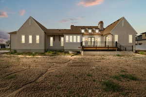 Back of property at dusk with a chimney and a deck