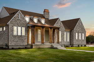 View of front of house with a chimney, a yard, a porch, and stone siding