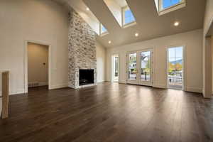 Unfurnished living room with a skylight, high vaulted ceiling, dark wood-type flooring, and a wealth of natural light