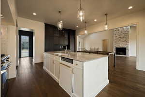 Kitchen with a kitchen island with sink, dark wood-style flooring, a sink, light stone counters, and range with gas stovetop