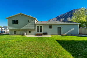 Rear view of property featuring fence, french doors, a patio area, a lawn, and a mountain view