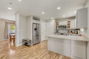 Kitchen with open shelves, a sink, light wood-style floors, stainless steel appliances, and a peninsula