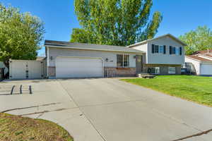 Tri-level home with a front yard, a gate, a garage, brick siding, and concrete driveway