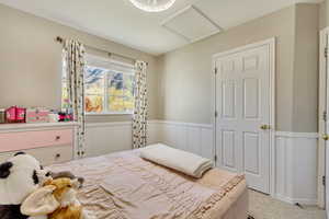 Bedroom with light colored carpet, attic access, and wainscoting