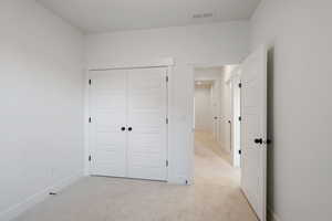 Unfurnished bedroom with visible vents, baseboards, a closet, and light colored carpet