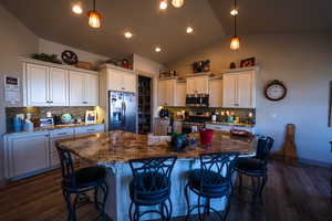 Kitchen with appliances with stainless steel finishes, backsplash, vaulted ceiling, and dark wood-style flooring