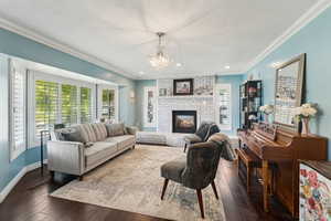 Living room featuring ornamental molding, dark wood-style flooring, a brick fireplace, a textured ceiling, and a notable chandelier