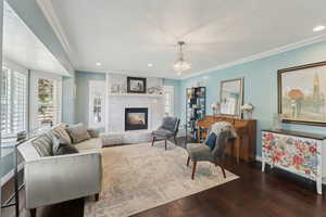 Living area with a brick fireplace, wood finished floors, baseboards, a chandelier, and ornamental molding