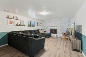 Living room with baseboards, a brick fireplace, wood finished floors, and visible vents