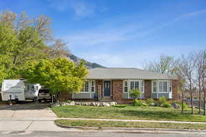 Ranch-style home with driveway, roof with shingles, brick siding, a mountain view, and a front lawn
