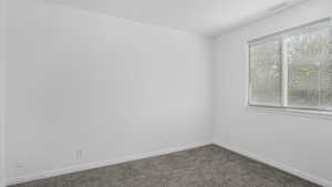 Empty room with baseboards, dark colored carpet, and visible vents