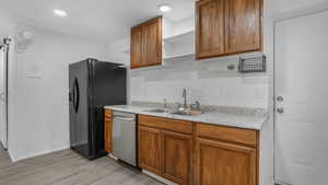 Kitchen with open shelves, stainless steel dishwasher, a sink, light wood finished floors, and black fridge