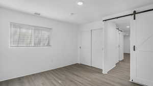 Unfurnished bedroom with a barn door, light wood-style flooring, recessed lighting, visible vents, and a closet
